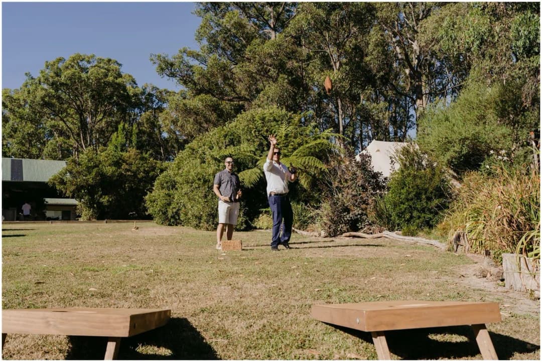 Two guests standing on the lawn near wooden ceremony benches.