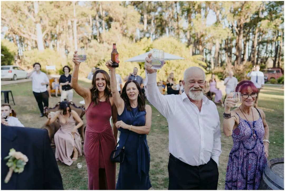 Guests raising drinks and cheering on the lawn.