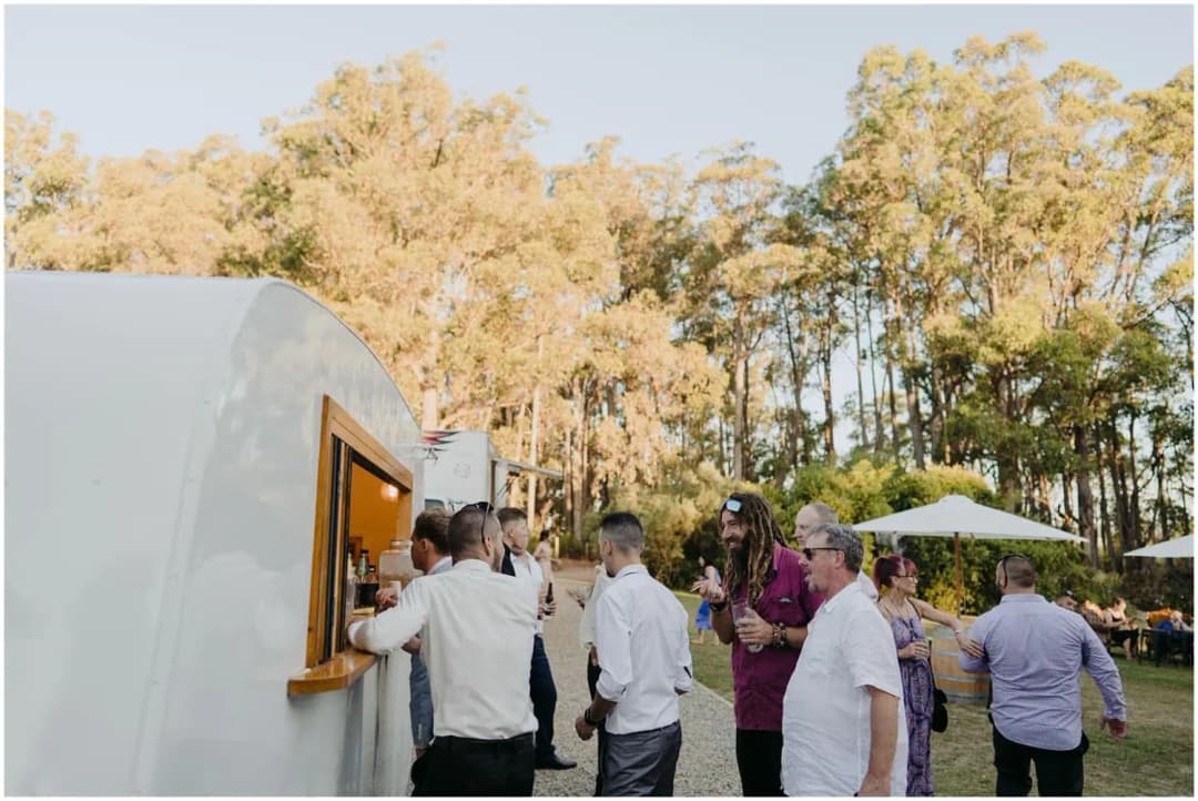 Guests gathered beside a white mobile bar outdoors.