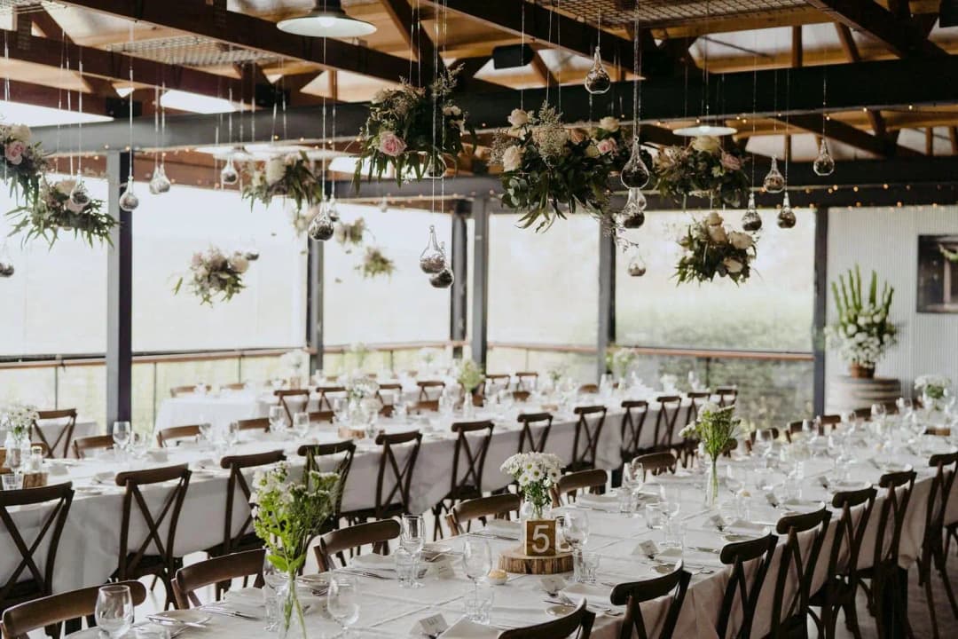 Reception tables beneath hanging plants and warm lights in a timber-roof room.
