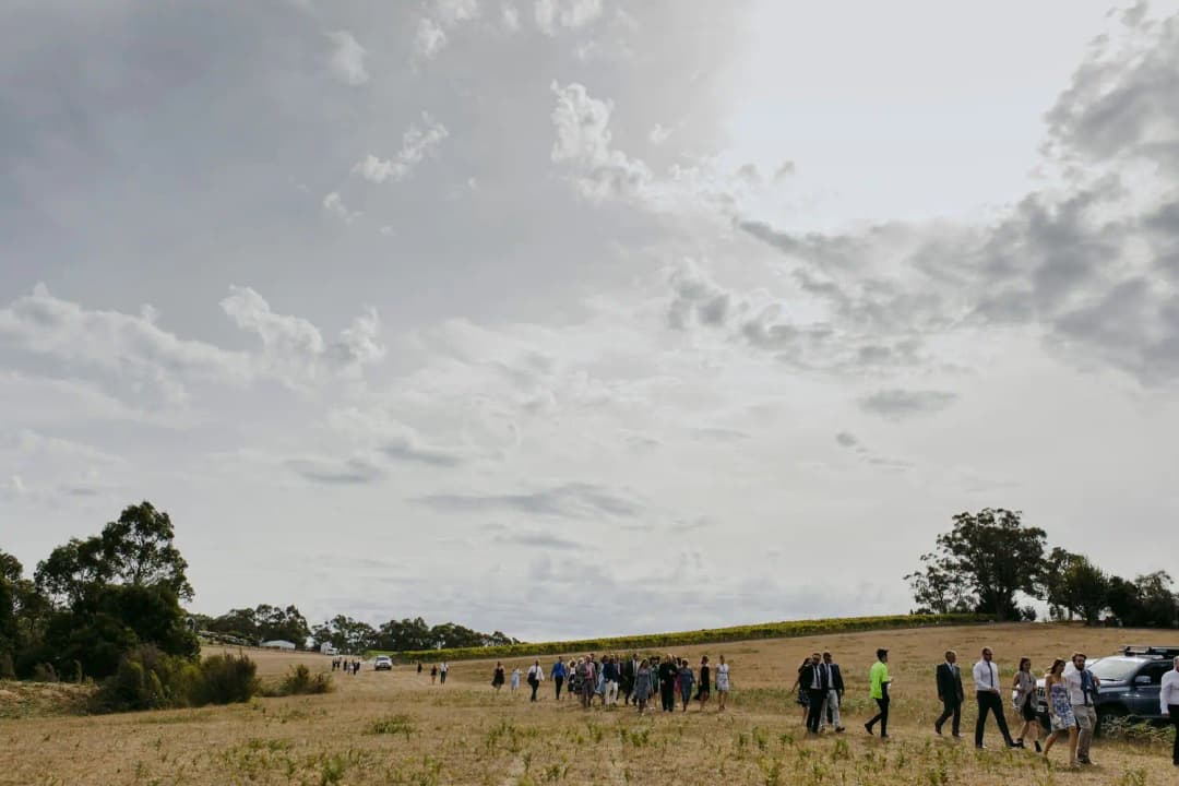 Guests walking across a field toward an outdoor ceremony beneath a cloudy sky.