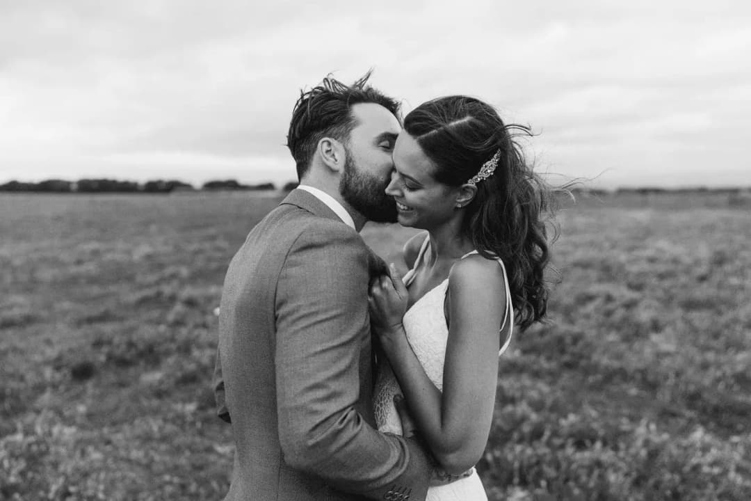 Black-and-white portrait of a couple embracing in a field.