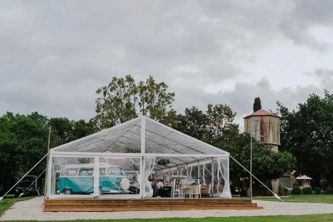 Clear marquee and vintage van on a lawn beside a water tower.