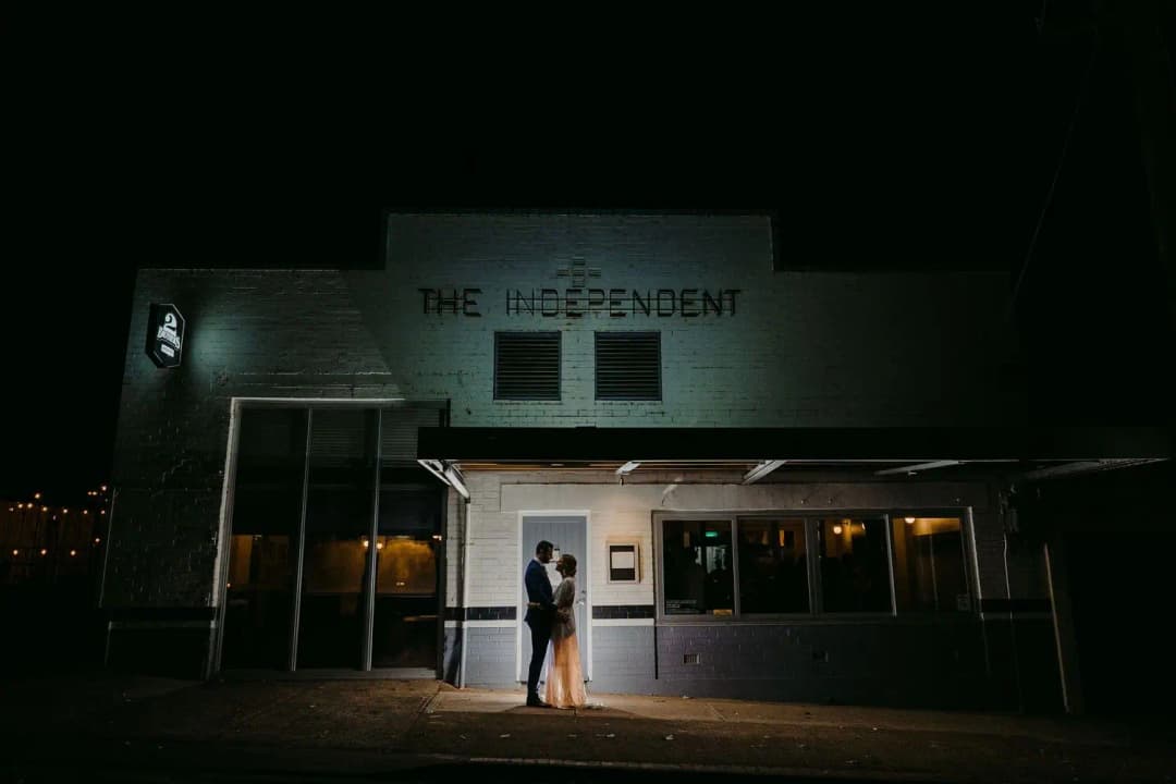 Couple standing in a lit doorway of a white restaurant building at night.