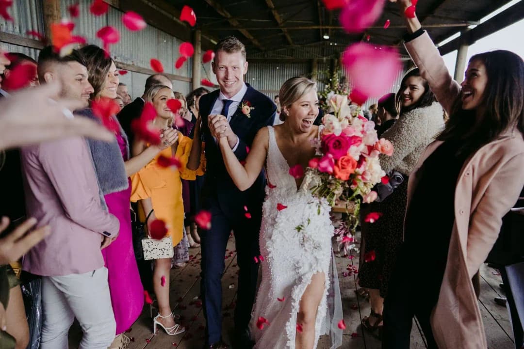Couple leaving the ceremony through guests throwing red rose petals.