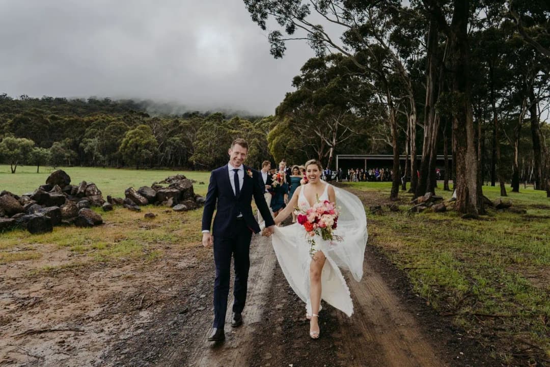 Couple walking hand in hand along a muddy track beside tall trees.