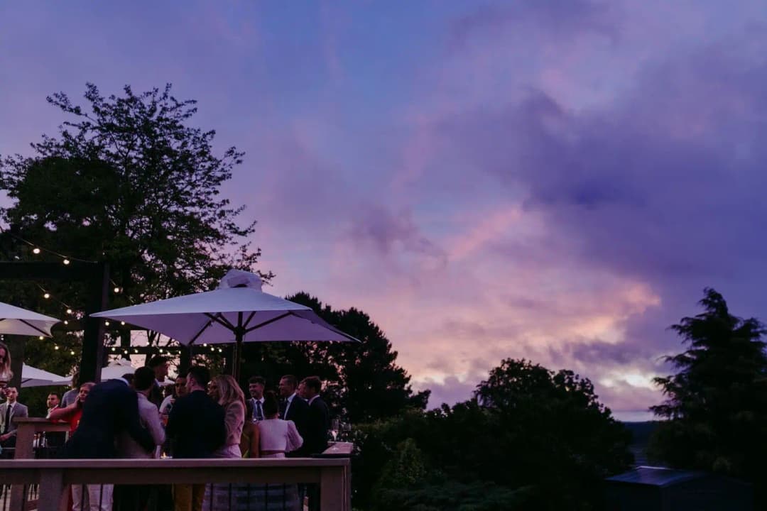 Purple and pink sunset clouds above guests on a reception terrace.