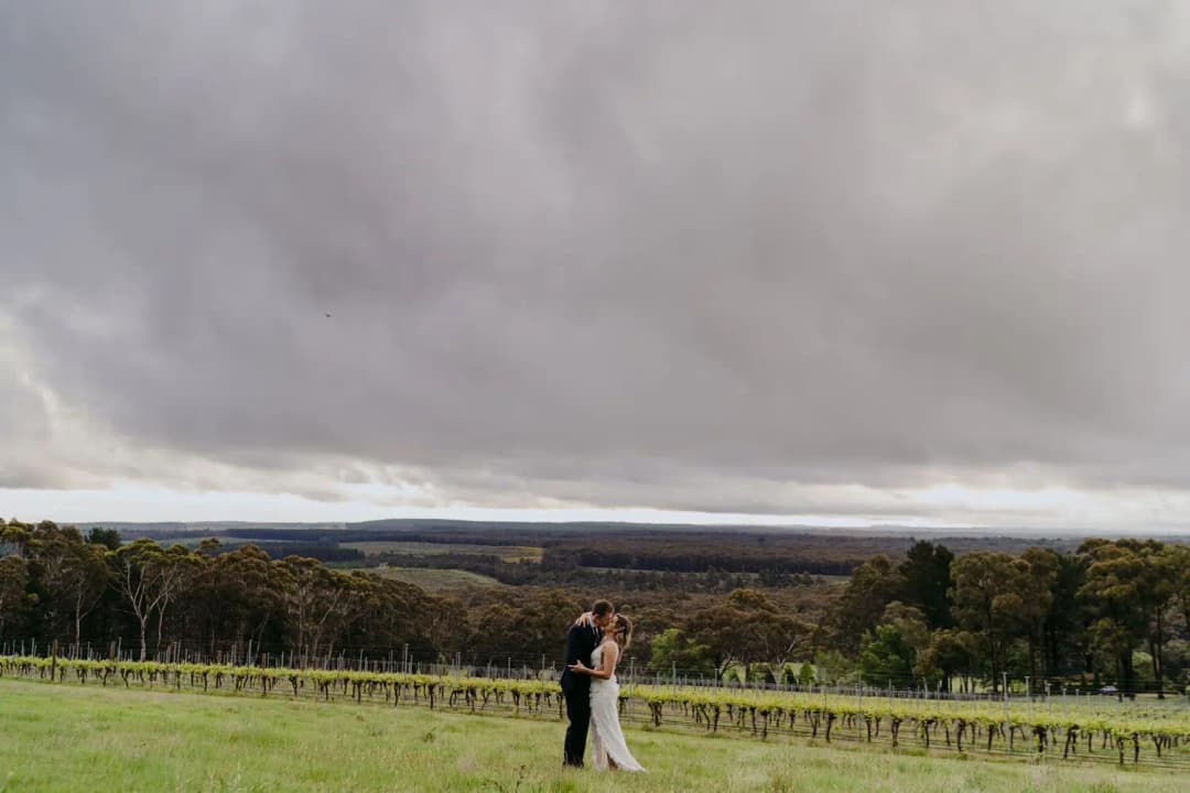 Couple embracing on a green hillside beneath heavy grey clouds.