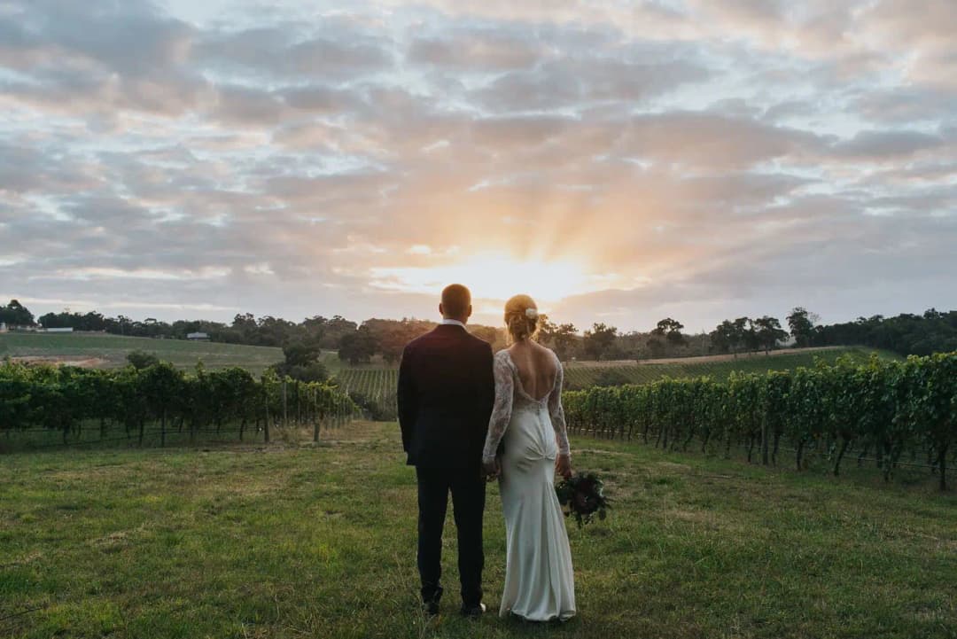 Couple embracing with their backs to the camera beneath sunset clouds.