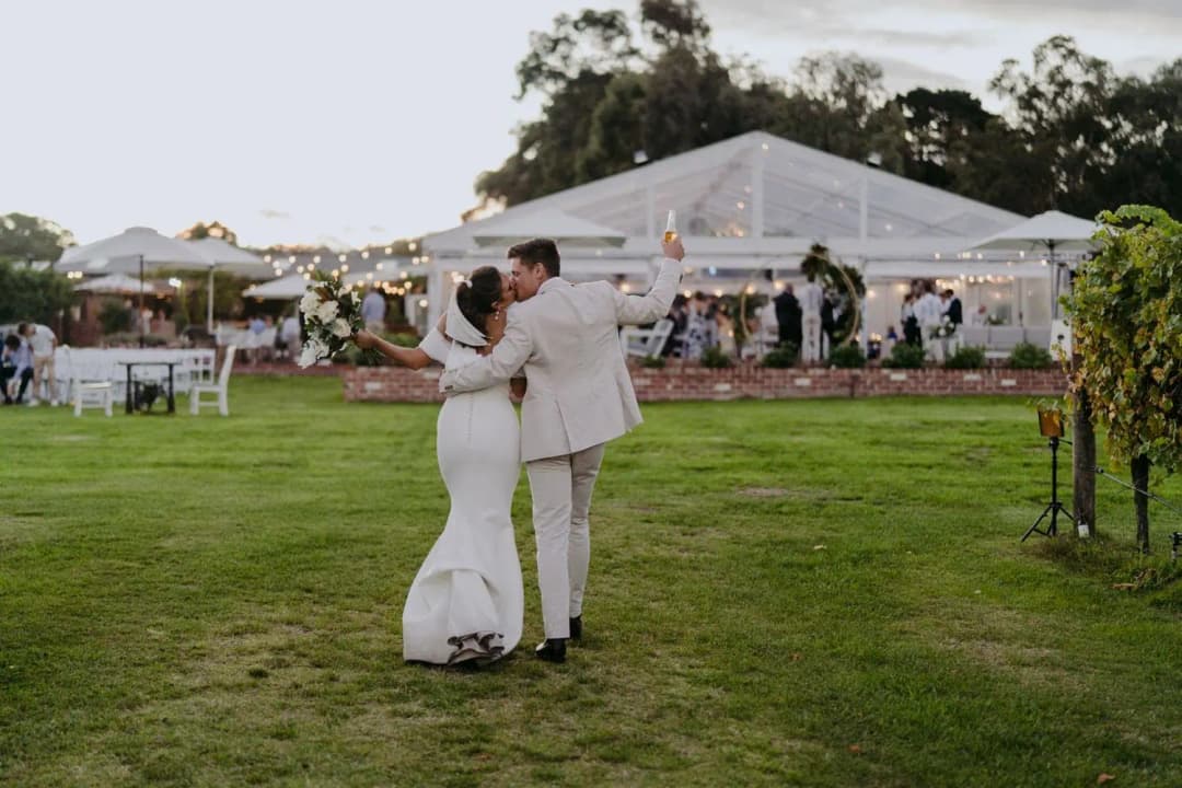 Groom dipping the bride on a lawn in front of a clear marquee.