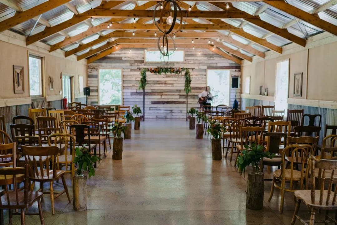 Rows of wooden chairs facing a ceremony arch beneath exposed timber roof beams.