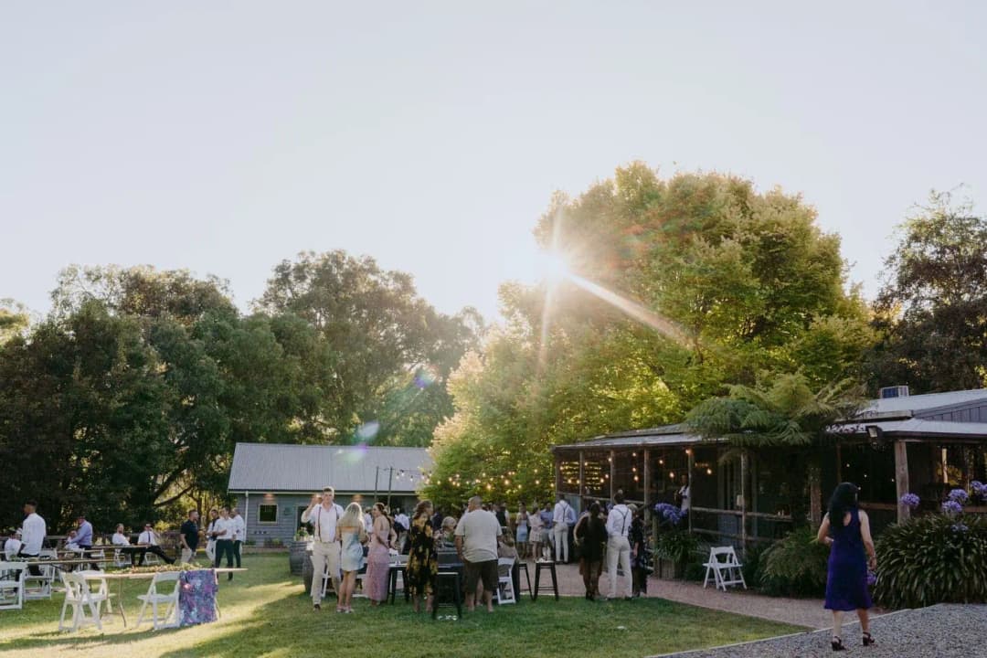 Guests gathered beside a timber reception building in warm evening light.