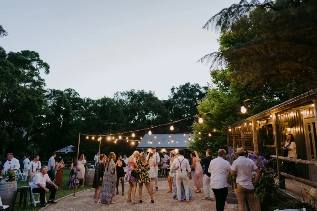 Guests dancing outside a timber building beneath string lights at dusk.