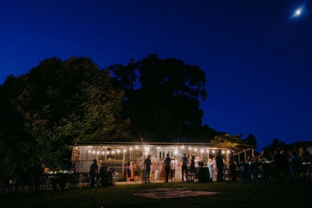 Illuminated timber reception building surrounded by dark trees at night.