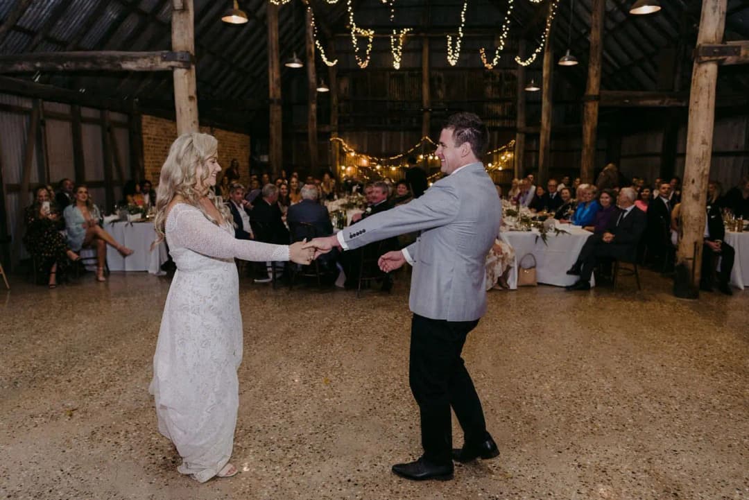 Bride and groom holding hands across the reception dance floor.