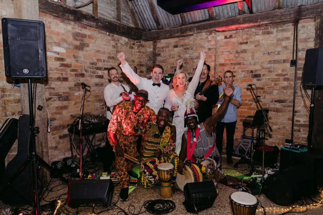 Bride and groom cheering with drummers and musicians among instruments and speakers.