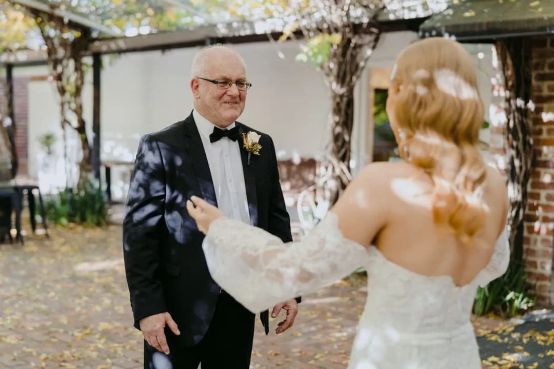 Bride greeting an older man in a dark suit beneath garden trees