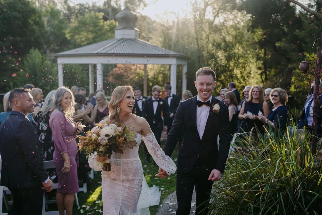 Newlyweds walking hand in hand from the gazebo as guests applaud