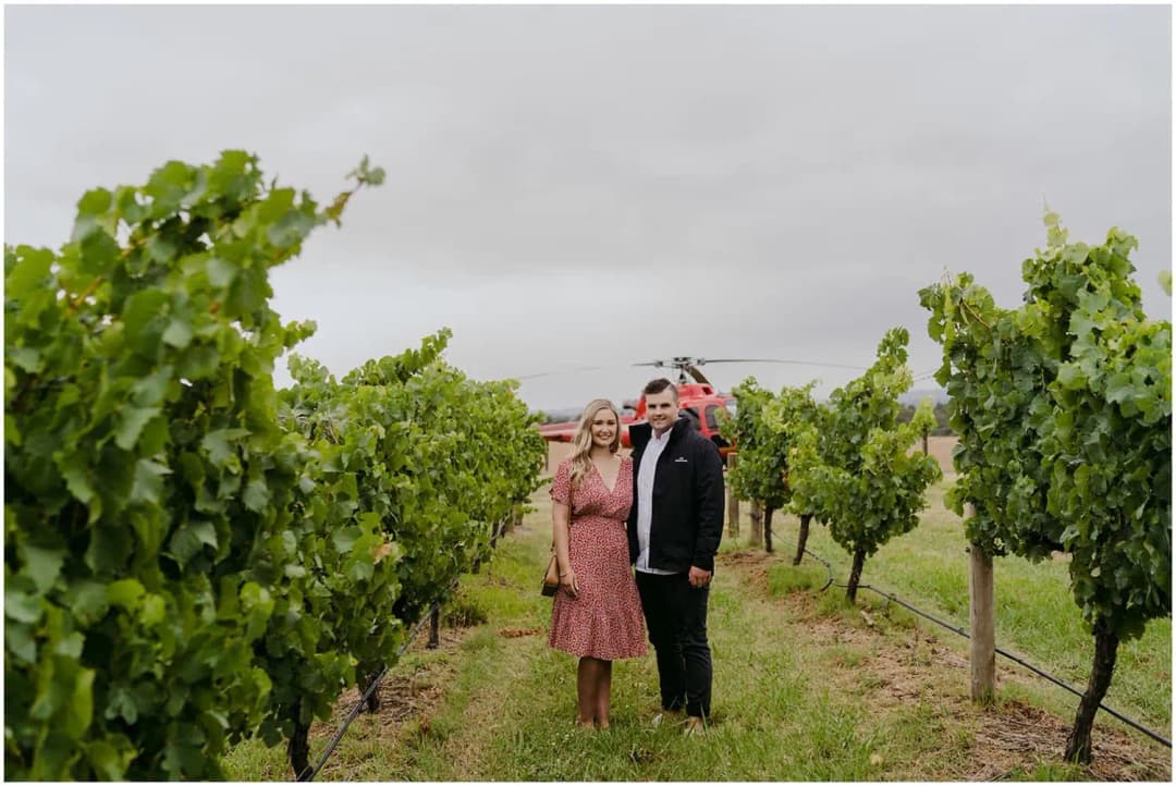 Couple standing together between green vineyard rows.