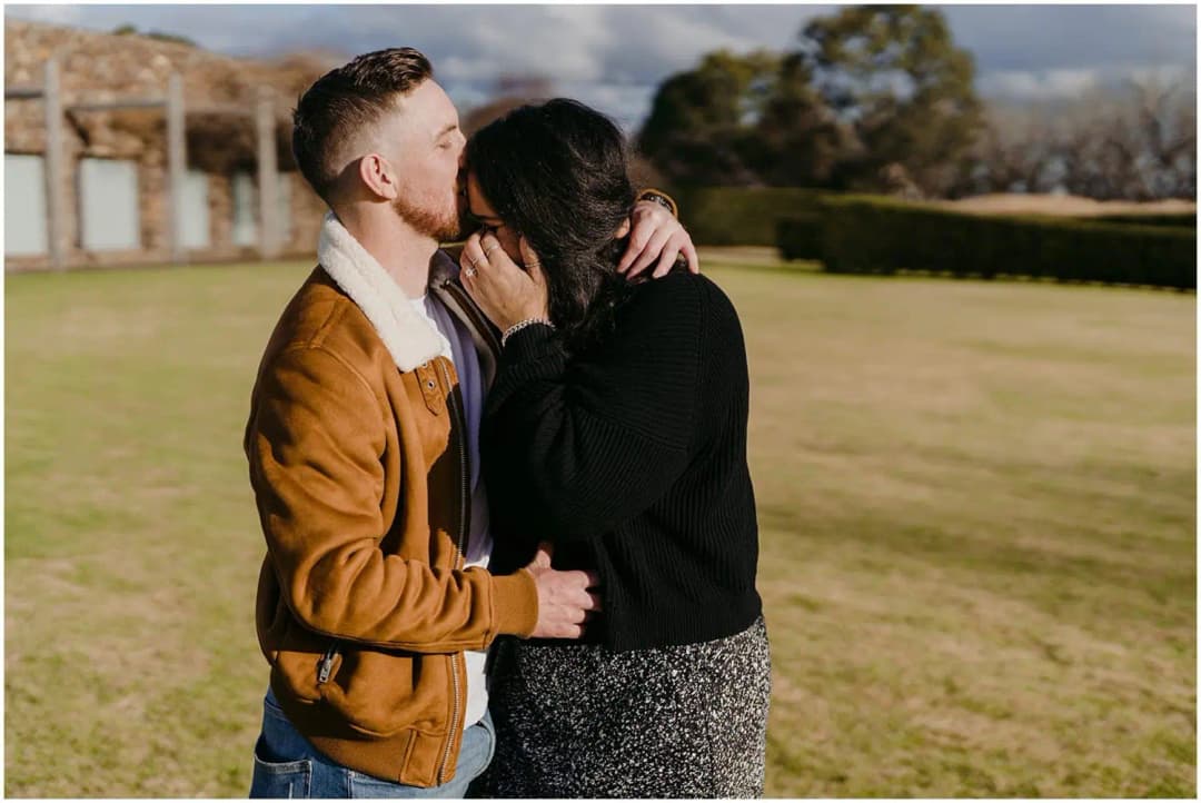 Couple embracing and kissing on a lawn in warm afternoon light.
