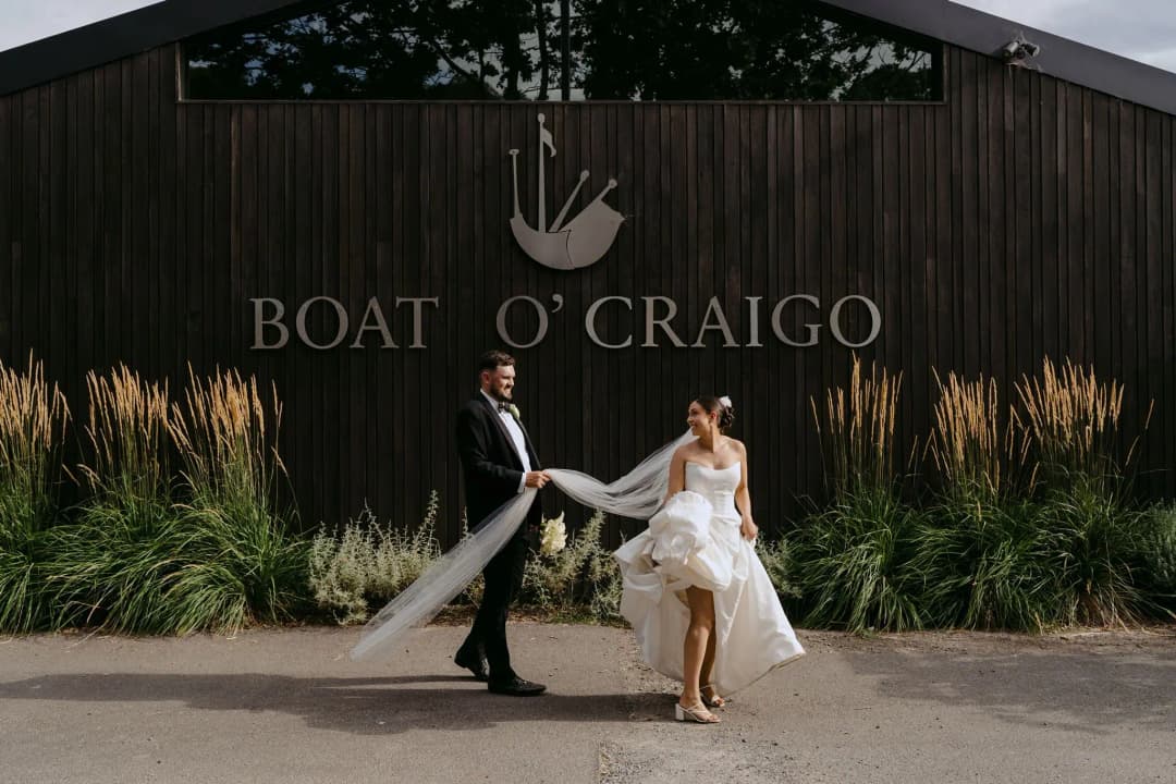 Couple holding hands outside a dark timber winery building.