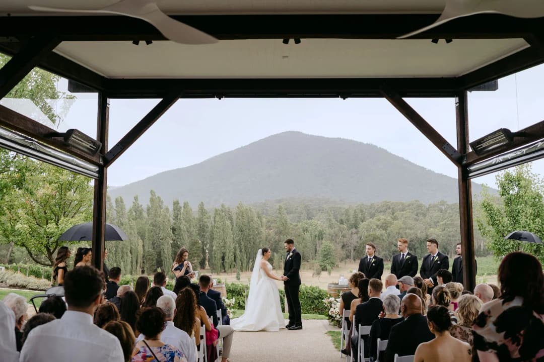 Guests watching an indoor ceremony through open doors overlooking a mountain.