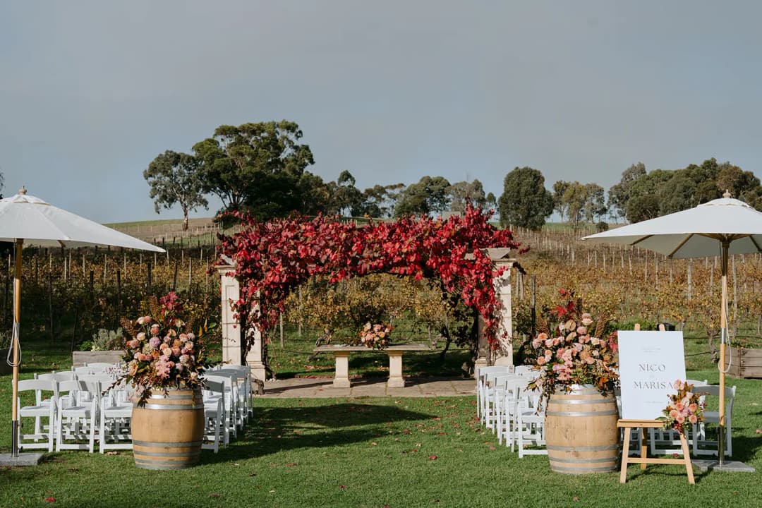 White ceremony chairs facing a pergola covered in red autumn leaves.