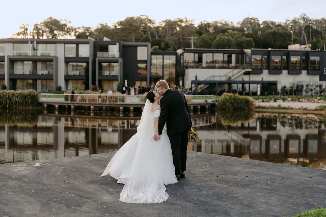 Couple embracing beside a reflecting pond in front of a modern building.