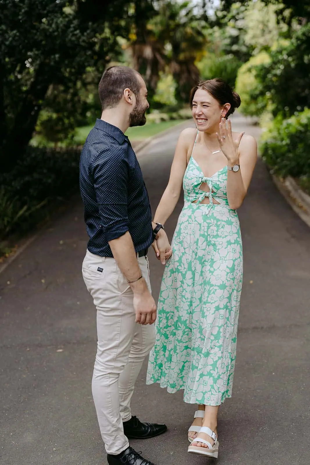 Couple holding hands on a garden path as the woman touches her face.