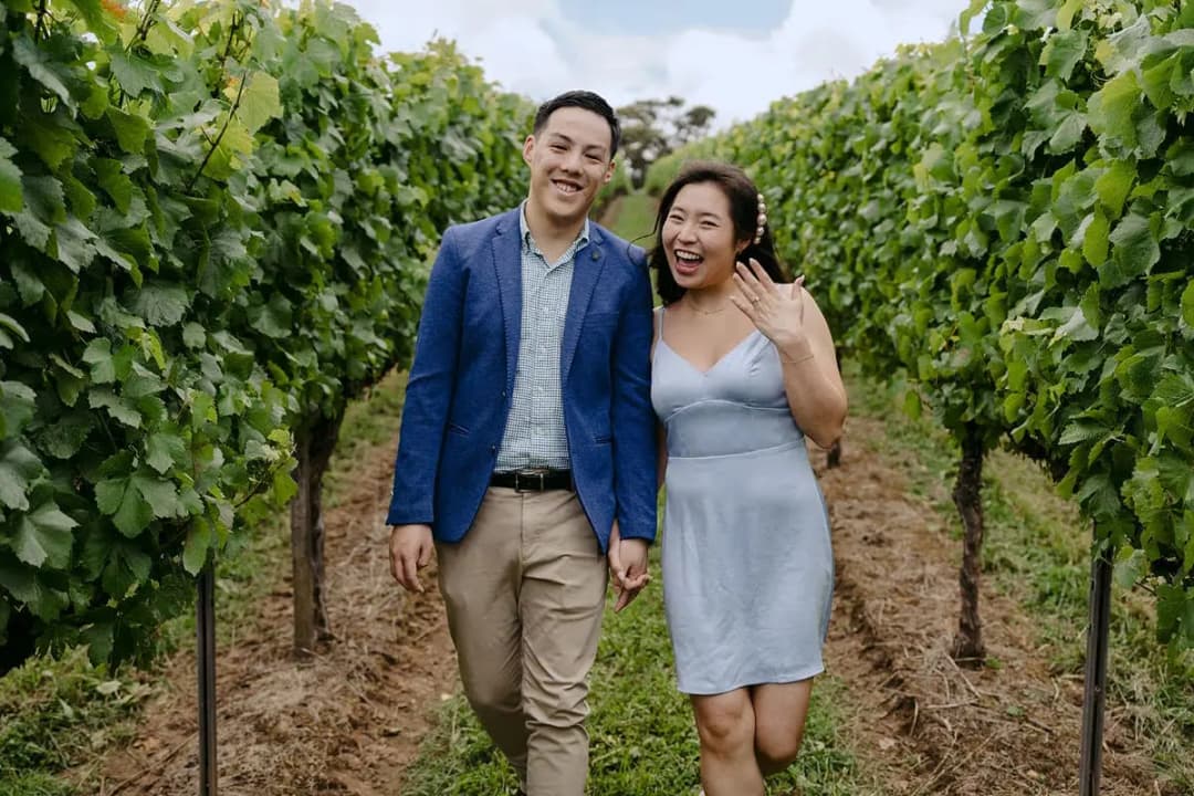 Couple smiling as they walk between leafy vineyard rows.