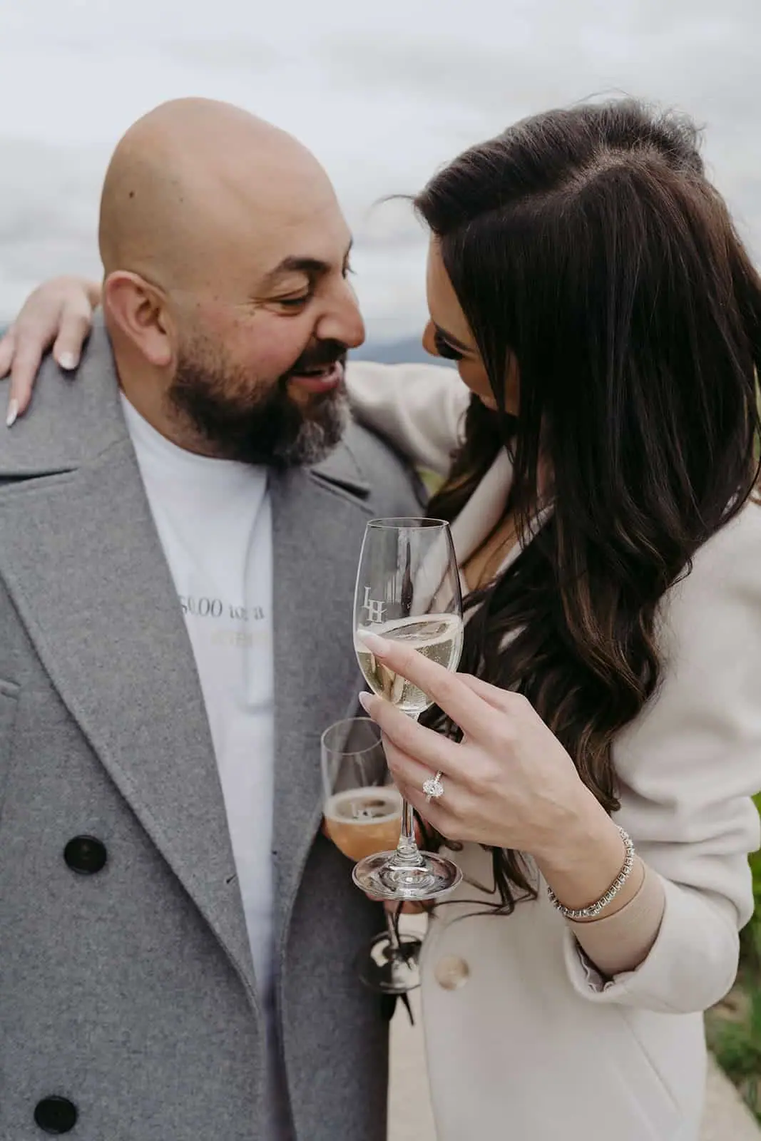 Couple smiling at each other while holding drinks outdoors.